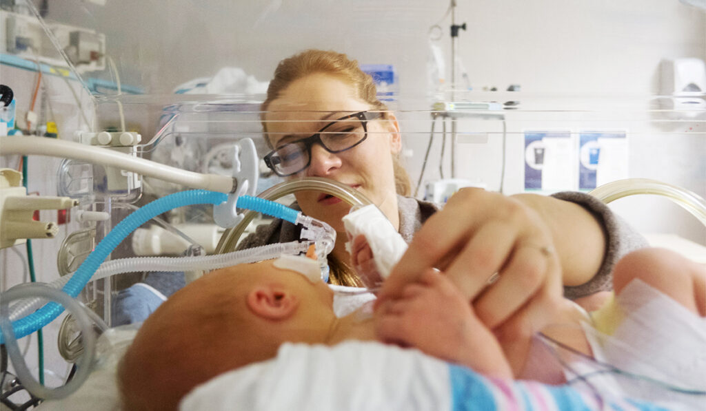 Woman holding finger of a baby in the NICU