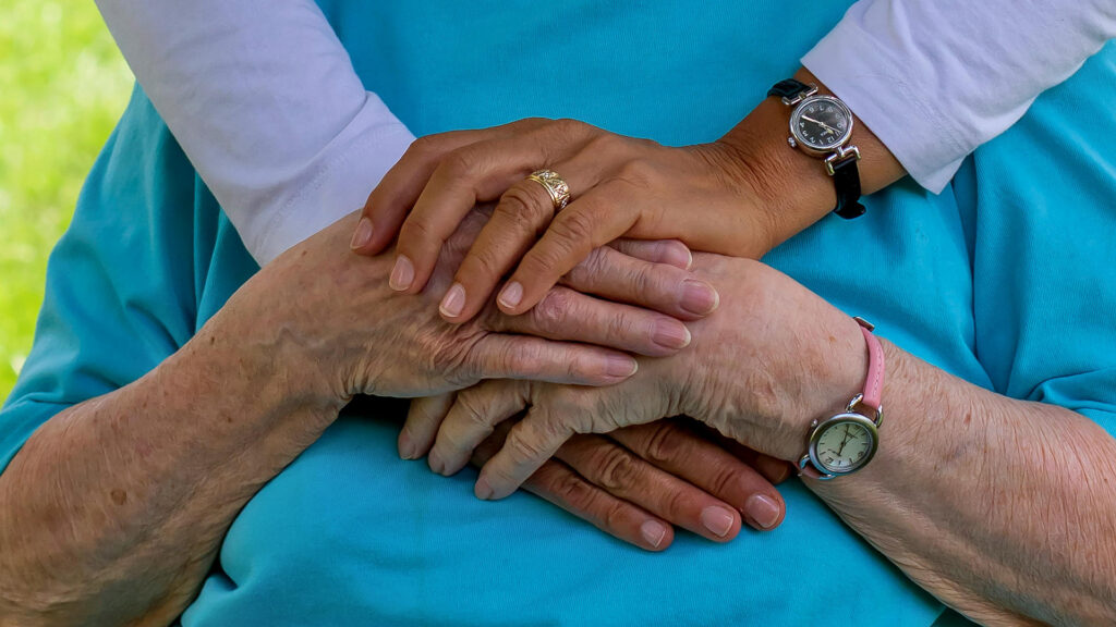 a younger woman places her hands on top of the hands of an older woman wearing a blue shirt