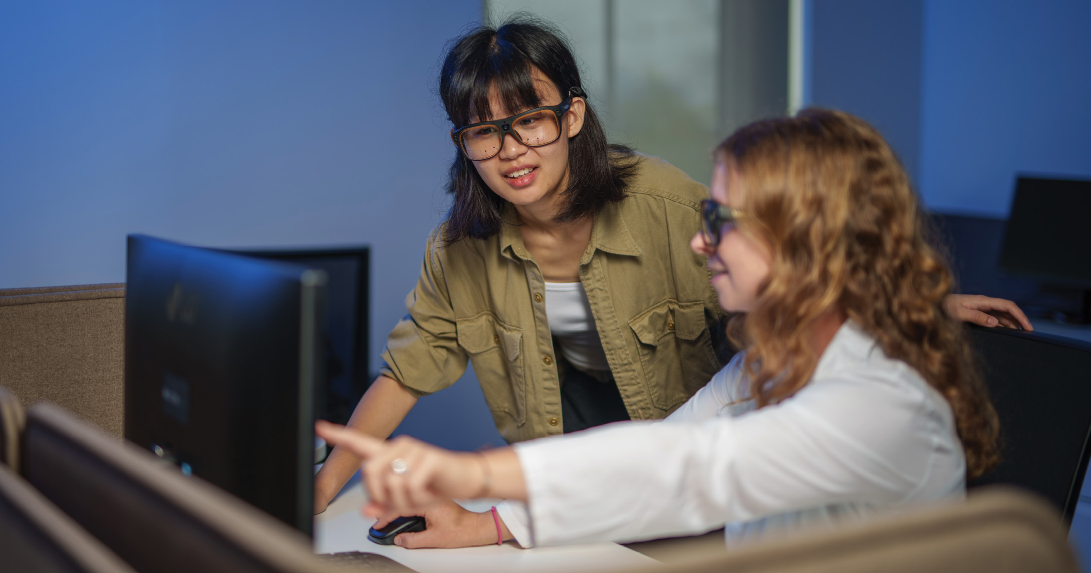 Two students wearing large glasses look at a computer screen.