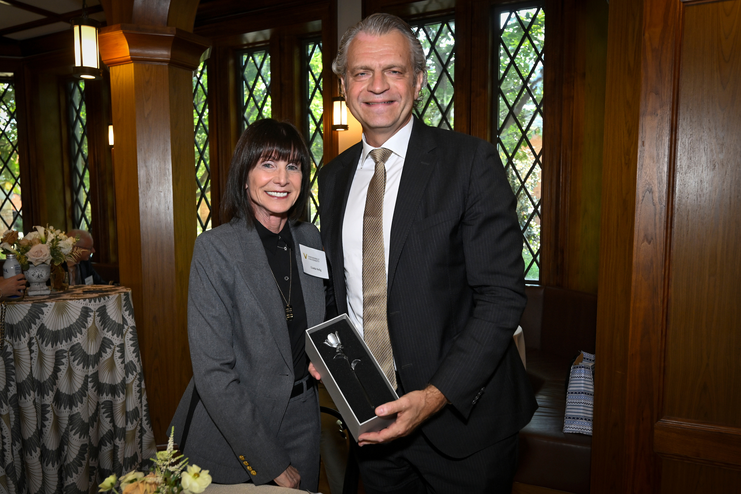 A man and a woman stand side by side, the man is holding a box with a white rose