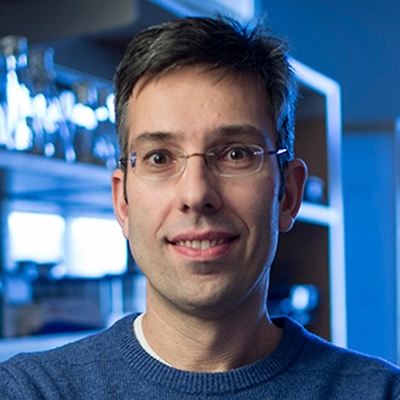 Antonis Rokas smiling in a blue background showcasing a lab bench