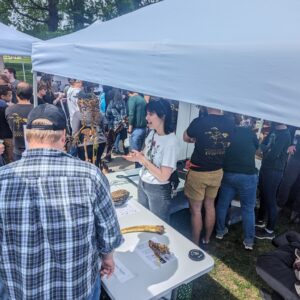 Allyson in a white tshirt standing under a tent explaining evolution to a person in a black shirt