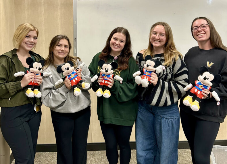 From left, SLP graduate students Leah Wirthlin, Sydney Lex, Abby Ragan, Bella Blanchet, and Sam Eason pose with adapted Mickey Mouse dolls at the Adaptive Toy Workshop. Photo by Emily Mathis.