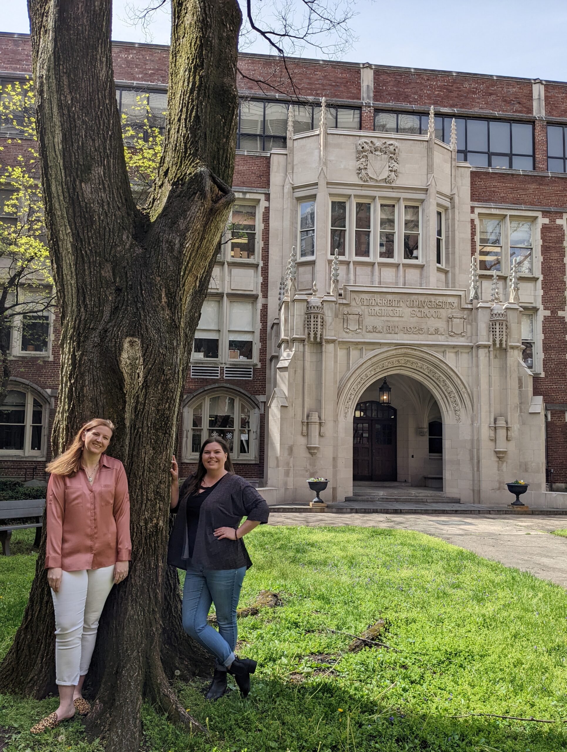 Megan and Sarah standing outside under a tree in front of a VUMC architectural entrance