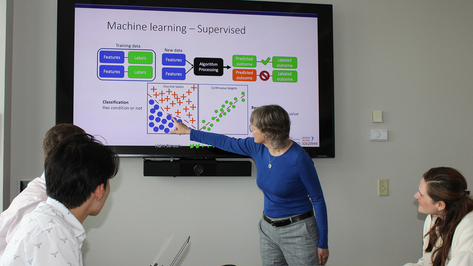 A VUSM faculty member points to a diagram of machine learning on a large screen during a presentation.