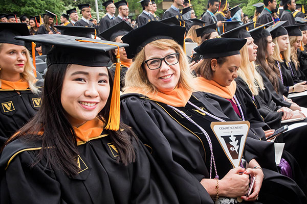 Rows of Vanderbilt graduates in gold and black robes sit waiting for Commencement to start. One is a master's graduate and the other is a doctor of nursing practice graduate.