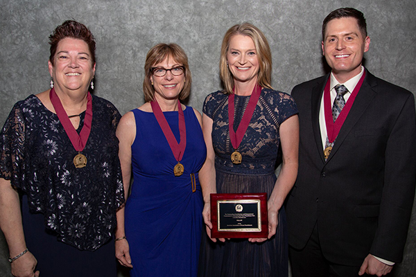 Four APRNs with AANP Fellows medals on ribbons around their next. 2018 inductee Jennifer Kim, holds a plaque.
