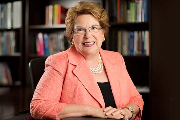 Dean Linda Norman in peach jacket in front of bookcase