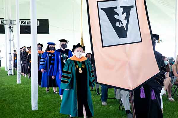 Vanderbilt Nursing faculty in academic regalia walk in procession behind the VUSN school banner